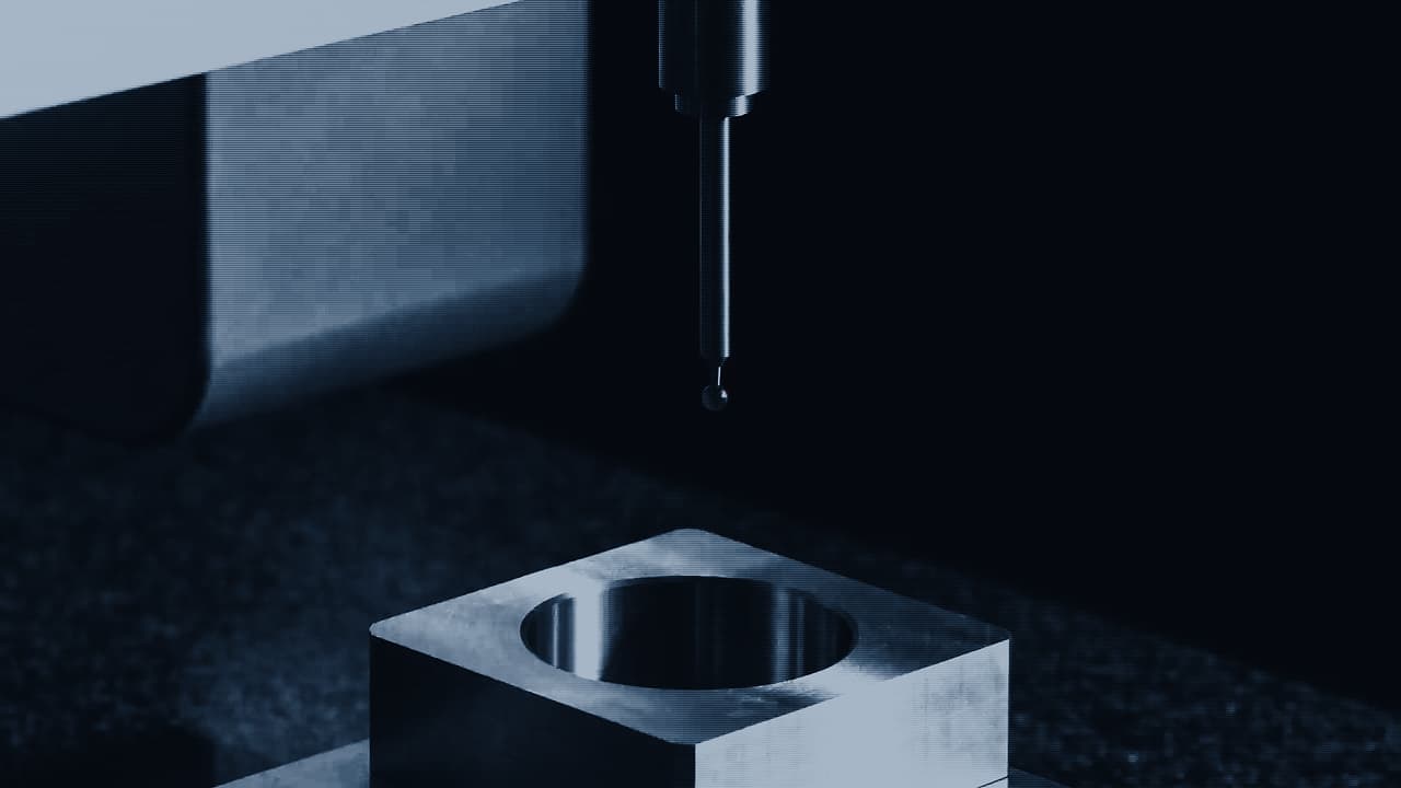A coordinate measuring machine probe lowered towards the bore of a machined steel housing on a granite table.