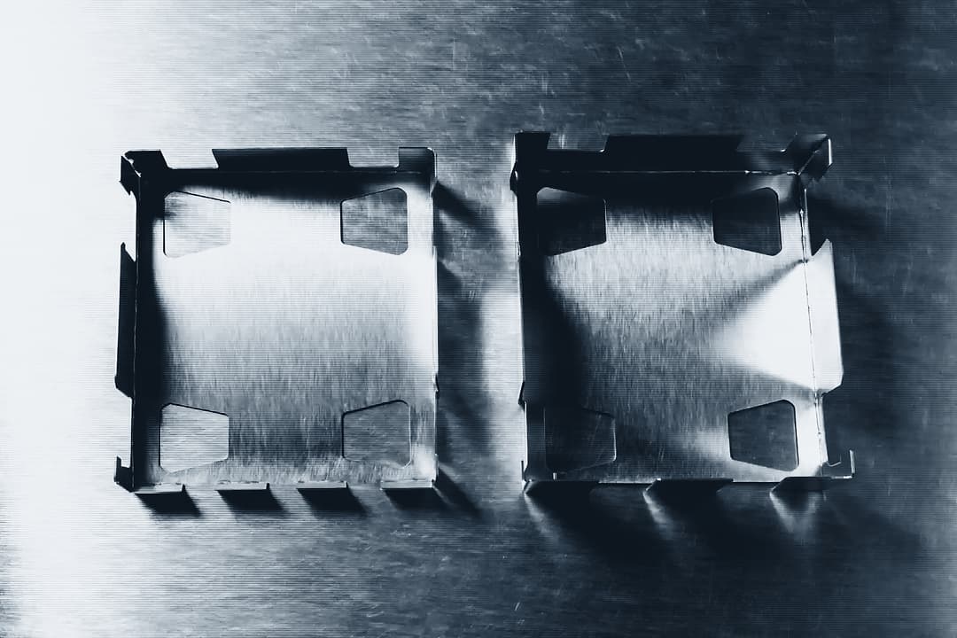 A laser-cut sheet metal flat pattern lying beside the same part folded into a finished enclosure, photographed from above on a steel bench.